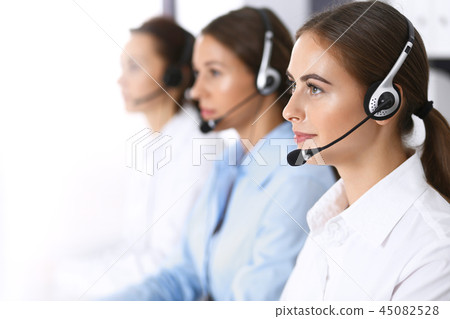 Group of callcenter operators at work. Focus at beautiful business woman in headset Group of callcenter operators at work. Focus at beautiful business woman in headset 45082528