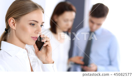 Serious blonde businesswoman talking by phone at the background of her colleagues in office Serious blonde businesswoman talking by phone at the background of her colleagues in office 45082577