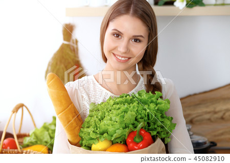 Young happy woman holding paper bag full of vegetables and fruits while smiling. Girl have made 45082910