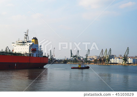 A small pilot ship leads a large red cargo ship 45103029