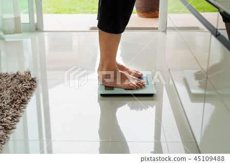 old woman standing on weight scale in living room 45109488