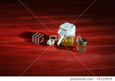 Honey in a glass jar close up on a black background on a red wooden table. pour honey with a stick Honey in a glass jar close up on a black background on a red wooden table. pour honey with a stick 45129939