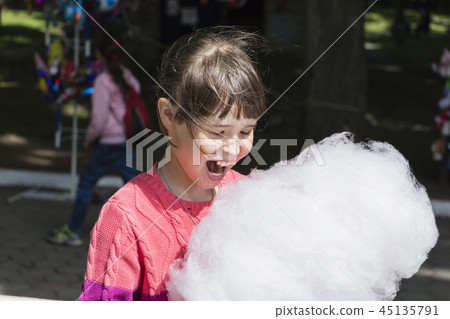 Young girl eating cotton candy in the park. 45135791