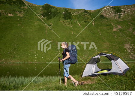 Woman tourist near camping in the mountains with backpack and trekking sticks in the morning 45139597