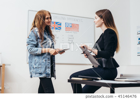 Two female students talking in classroom. College, English language school. 45146476