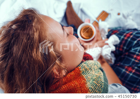 View from above on sick woman in bed holding a cup of tea with orange in it View from above on sick woman in bed holding a cup of tea with orange in it 45150730