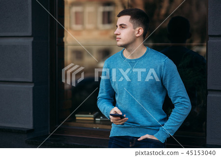 Young man is using the phone on the street. Handsome guy stand in front of window 45153040