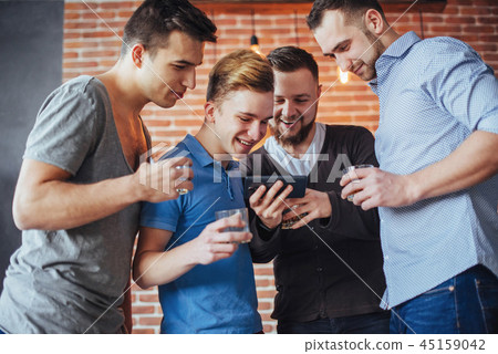 Cheerful old friends communicate with each other and phone watch,  glasses of whiskey in pub. Concep 45159042
