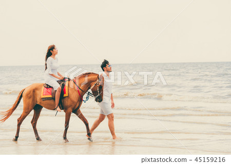 Young couple goes horse riding on tropical beach. 45159216