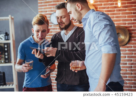 Cheerful old friends communicate with each other and phone watch,  glasses of whiskey in pub. Concep 45159423