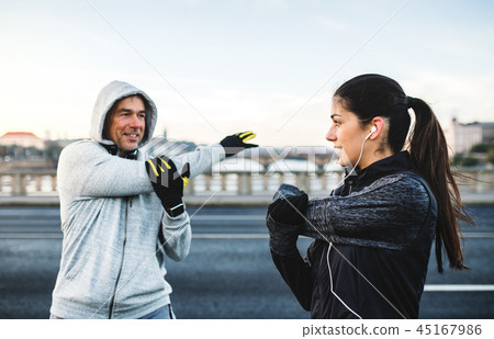 A fit couple runers doing stretching outdoors on the bridge in Prague city. A fit couple runers doing stretching outdoors on the bridge in Prague city. 45167986