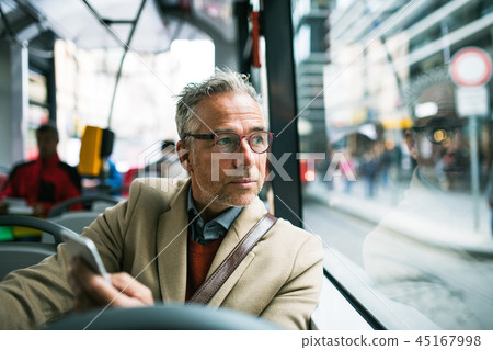 Mature businessman with smartphone travelling by bus in city. Mature businessman with smartphone travelling by bus in city. 45167998