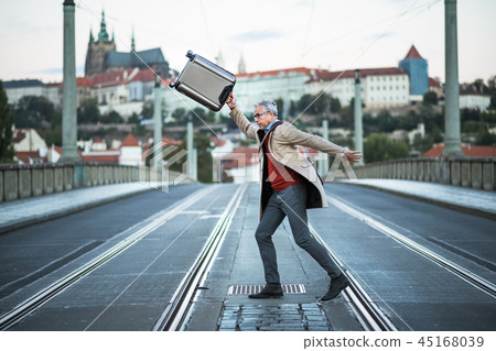 A happy mature businessman with suitcase crossing a road in Prague city. A happy mature businessman with suitcase crossing a road in Prague city. 45168039