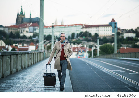 Mature businessman with suitcase walking on a bridge in Prague city. 45168040