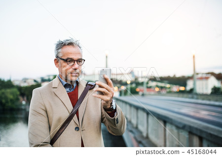 Mature businessman with smartphone standing by river in Prague city, taking selfie. Mature businessman with smartphone standing by river in Prague city, taking selfie. 45168044
