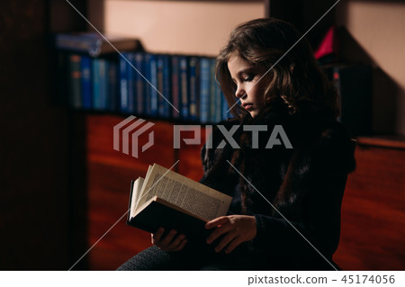 Beautiful little girl is reading a book in the library. 45174056