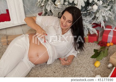 beautiful pregnant woman at the Christmas tree with gifts for the new year beautiful pregnant woman at the Christmas tree with gifts for the new year 45177890