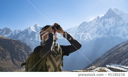 Hiker looking through binoculars on a trekking trail to the Annapurna base camp, the Himalayas 45180238
