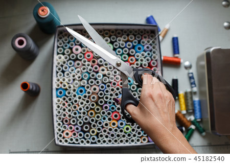 A seamstress pulls a pair of scissors out of a box with skeins of colored threads.Sewing industry A seamstress pulls a pair of scissors out of a box with skeins of colored threads.Sewing industry 45182540