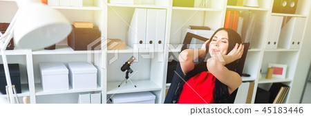 Beautiful young girl in headphones sits in the office at the table. Beautiful young girl in headphones sits in the office at the table. 45183446