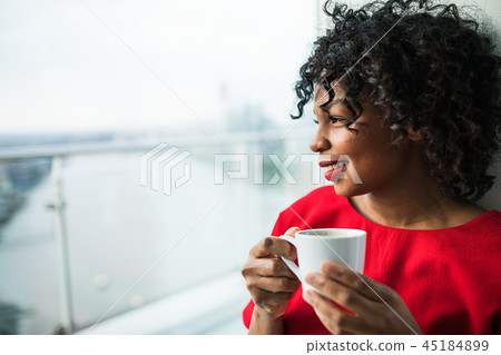 A close-up of a woman standing by the window holding a cup of coffee. A close-up of a woman standing by the window holding a cup of coffee. 45184899