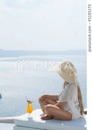 young woman drinking a cocktail enjoying a magnificent view of Santorini near the pool 45185274