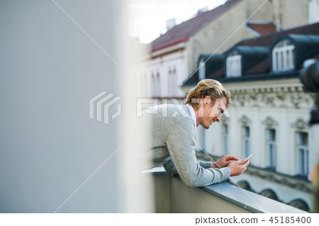 Young man with smartphone standing on a balcony in city, texting. Young man with smartphone standing on a balcony in city, texting. 45185400