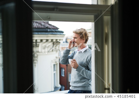 Young man with smartphone standing on a balcony in city, making a phone call. Young man with smartphone standing on a balcony in city, making a phone call. 45185401