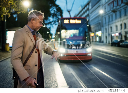 Mature businessman with suitcase waiting for a tram in the evening. Mature businessman with suitcase waiting for a tram in the evening. 45185444