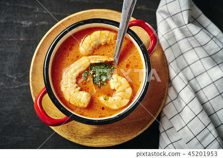 traditional Thai soup with shrimp in a red pot and a spoon with parsley traditional Thai soup with shrimp in a red pot and a spoon with parsley 45201953