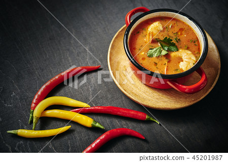 traditional Thai soup with shrimp in a red pot with parsley and chilli pepper traditional Thai soup with shrimp in a red pot with parsley and chilli pepper 45201987