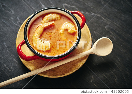 traditional Thai soup with shrimp in a red pot and a wooden spoon traditional Thai soup with shrimp in a red pot and a wooden spoon 45202005