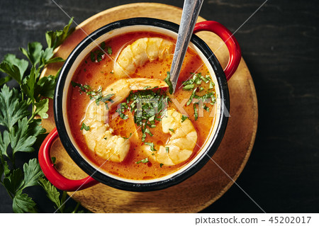 traditional Thai soup with shrimp in a red pot and a spoon with parsley traditional Thai soup with shrimp in a red pot and a spoon with parsley 45202017