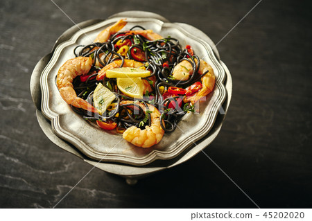 fresh, delicious black spaghetti with grilled prawns, tomatoes, chilli on an old silver plate fresh, delicious black spaghetti with grilled prawns, tomatoes, chilli on an old silver plate 45202020