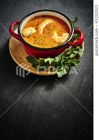 traditional Thai soup with shrimp in a red pot with parsley traditional Thai soup with shrimp in a red pot with parsley 45202022