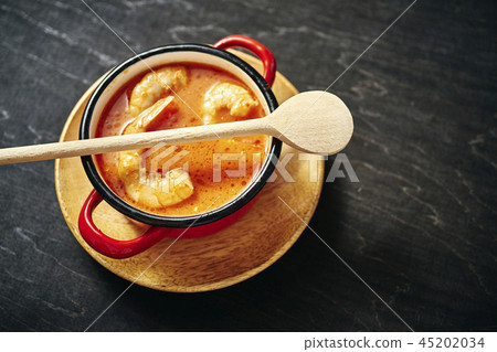 traditional Thai soup with shrimp in a red pot and a wooden spoon traditional Thai soup with shrimp in a red pot and a wooden spoon 45202034
