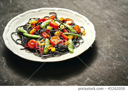 fresh delicious black vegan spaghetti with tomatoes, chili pepper, on a white plate fresh delicious black vegan spaghetti with tomatoes, chili pepper, on a white plate 45202050