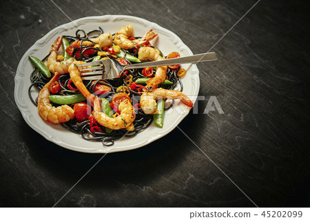 fresh, delicious black spaghetti with grilled shrimps, tomatoes, chilli, on a white plate fresh, delicious black spaghetti with grilled shrimps, tomatoes, chilli, on a white plate 45202099