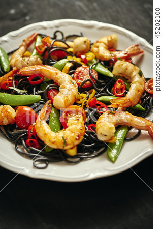 fresh, delicious black spaghetti with grilled shrimps, tomatoes, chilli, on a white plate fresh, delicious black spaghetti with grilled shrimps, tomatoes, chilli, on a white plate 45202100