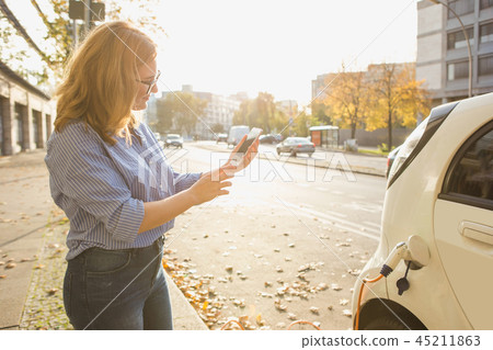 Young woman is standing near the electric car  45211863