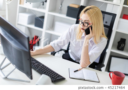 A young girl working at a computer in the office and talking on the phone. 45217464
