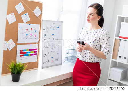 Young girl standing in the office near the Board with stickers and holding a phone. 45217492