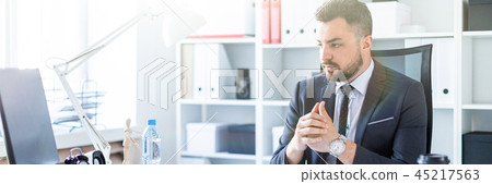 A man sits in a chair in the office at the table and looks at the monitor. A man sits in a chair in the office at the table and looks at the monitor. 45217563