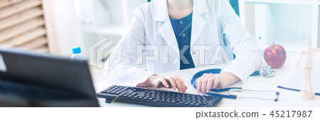 A beautiful young girl in a white robe is sitting at the table and typing on the keyboard. 45217987