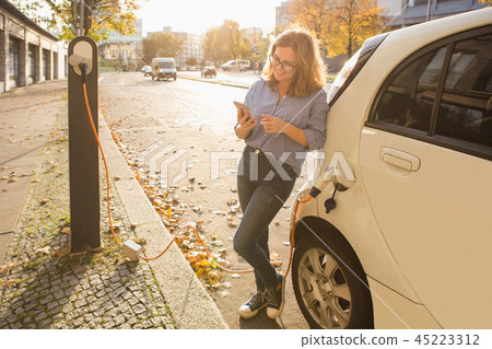Young woman is standing near the electric car  45223312