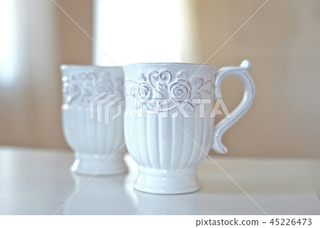 Set of white ceramic kitchen utensils, dishes on white table in big bright room infront of window. Set of white ceramic kitchen utensils, dishes on white table in big bright room infront of window. 45226473