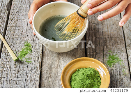 Matcha green tea accessoires on the rough wooden boards with girl's hands preparing matcha tea in a Matcha green tea accessoires on the rough wooden boards with girl's hands preparing matcha tea in a 45231179