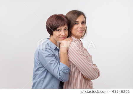 Beautiful maturesenior mom and her adult daughter are hugging, looking at camera and smiling. Beautiful maturesenior mom and her adult daughter are hugging, looking at camera and smiling. 45246201