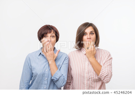 Portrait of a two surprised women mature mother and daughter standing over gray background and 45246204