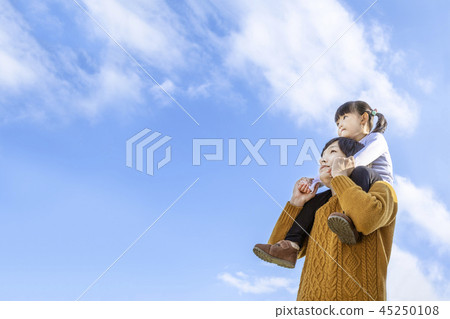 A father who shoulders his daughter and looks up at a distance against a blue sky. Family, parent and child, happiness, affection image 45250108